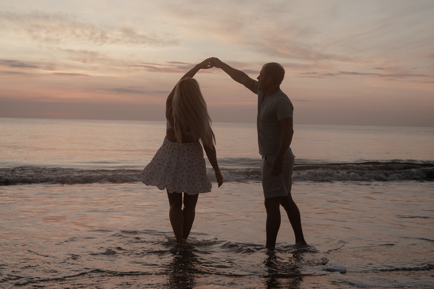 Couple playing in the waves with reflections on the wet sand