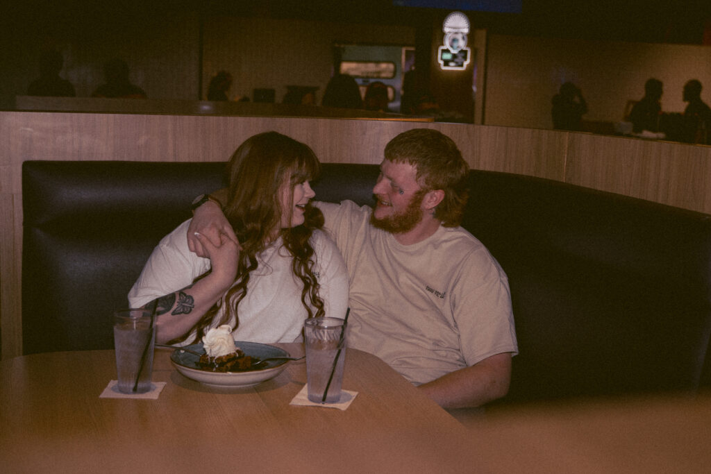 Couple laughing together in a diner booth during candid engagement photos